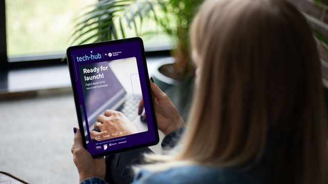 Person holding a tablet displaying the Tech Hub digital starter kit with a blurred background of a window and plant.
