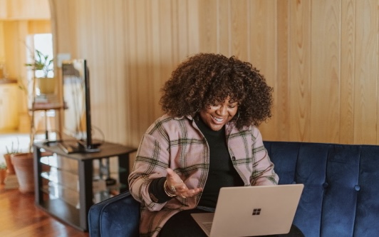 Image of woman sat on a sofa with a laptop on her lap, smiling