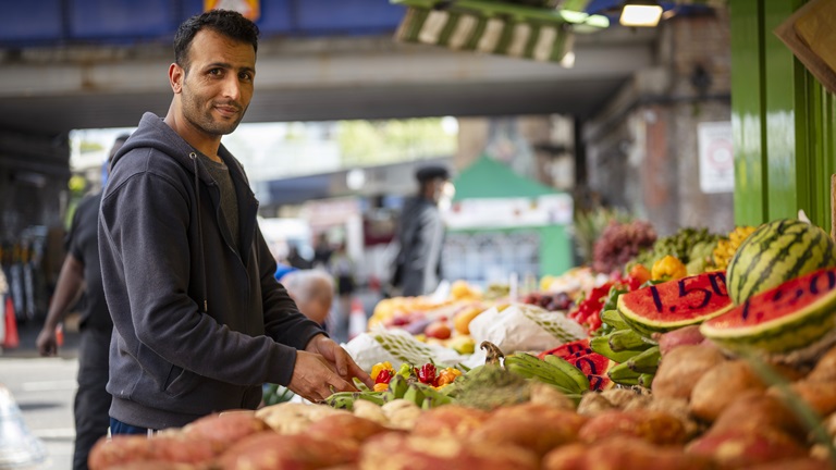 A male Middle Eastern grocer organises the fruit and vegetables on his market stall